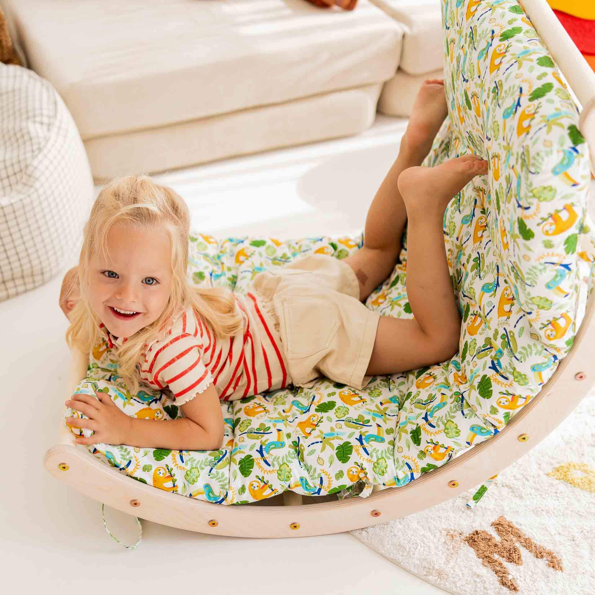 Fröhliches Kind auf einem Holz-Kletterbogen mit buntem Kissen, das zum Spielen einlädt.