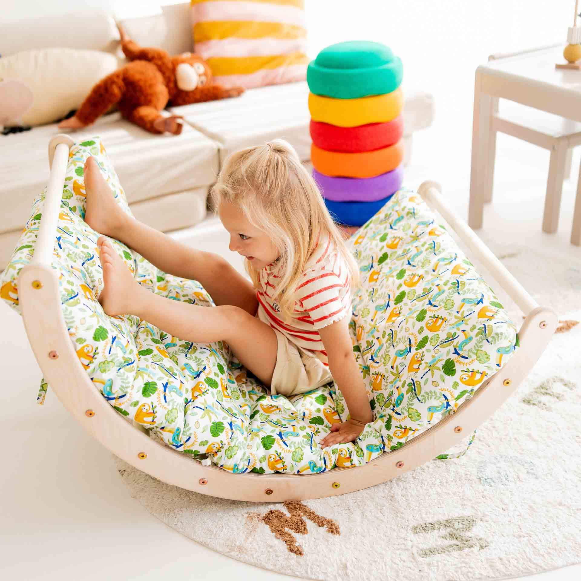 Kind auf einem Kletterbogen Basic mit buntem Kissen, umgeben von Spielzeug, für Spaß und Bewegung.