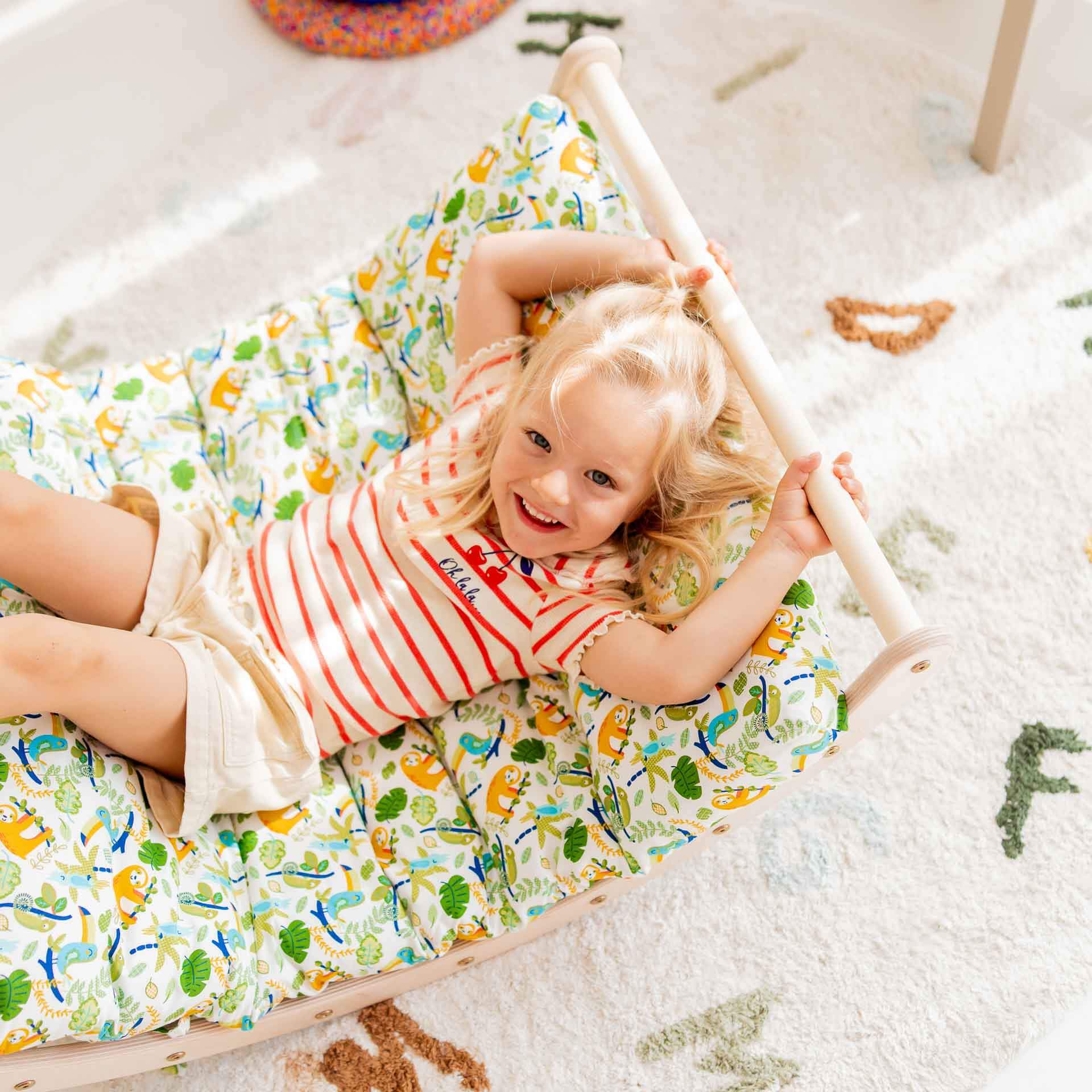 Glückliches Kind, das auf einem Kletterbogen mit buntem Polster liegt, das Spaß beim Spielen hat.