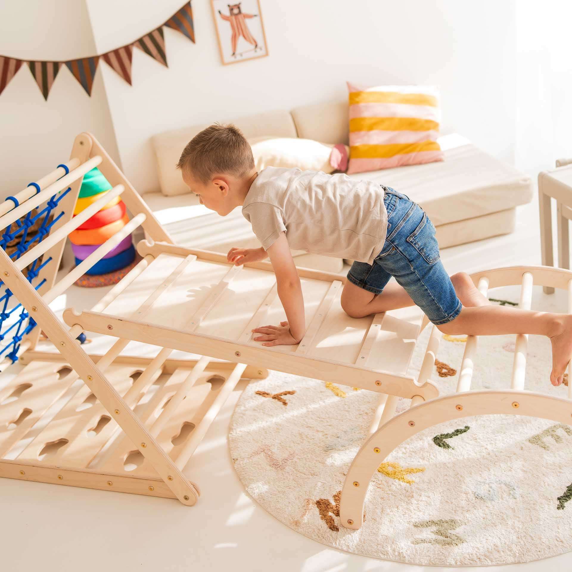 Ein Junge klettert fröhlich auf einem Kletterbogen aus Holz in einem hellen Spielzimmer. Der Bogen fördert Bewegungsfähigkeiten.