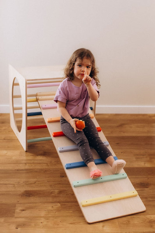 Kletterwürfel versch. Farben mit einem Kind, das auf der Rutsche sitzt und einen Snack genießt.