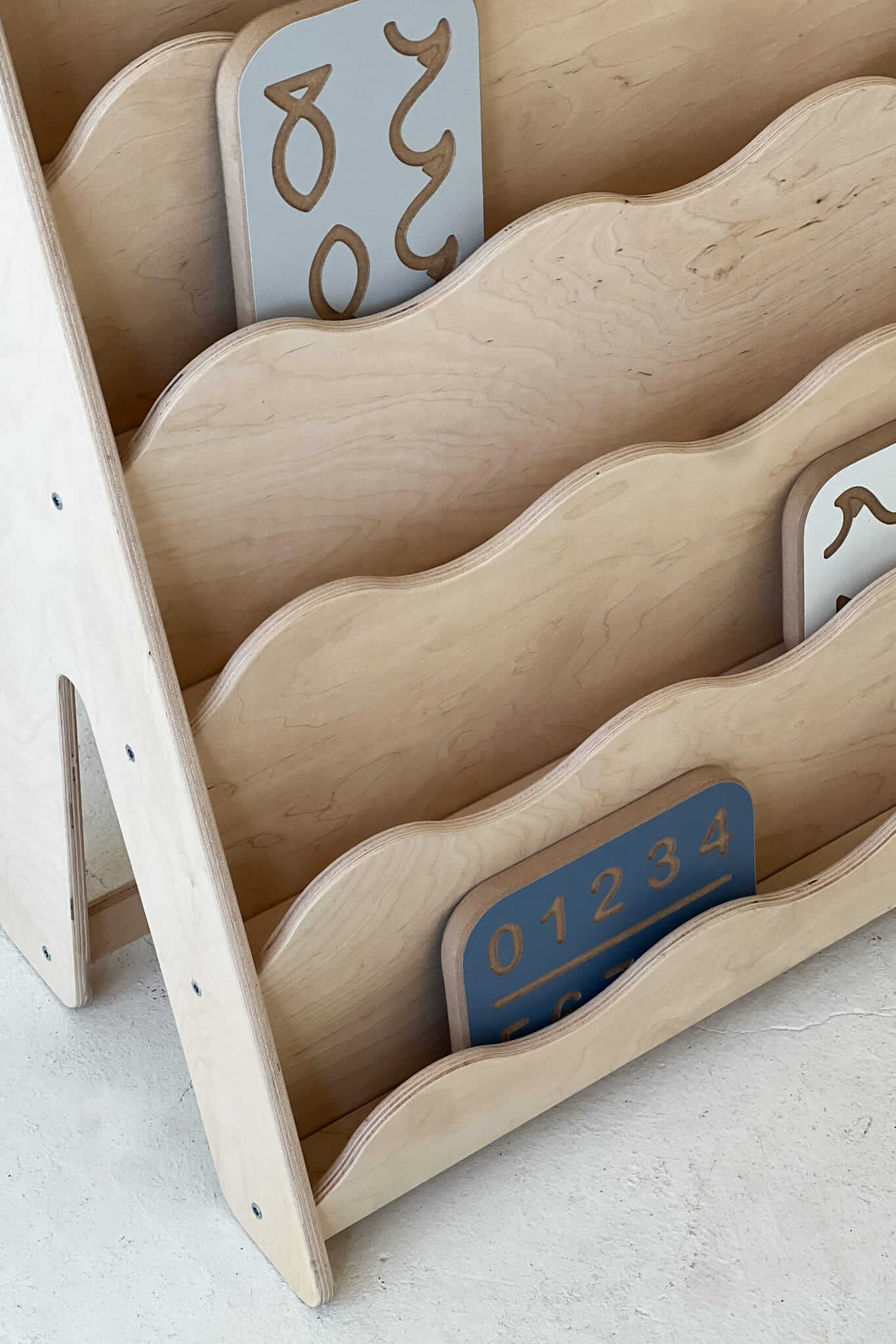 Bücherregal Wave für Kinder aus Holz mit Wellenlinien und sichtbaren, einladenden Buchkarten.