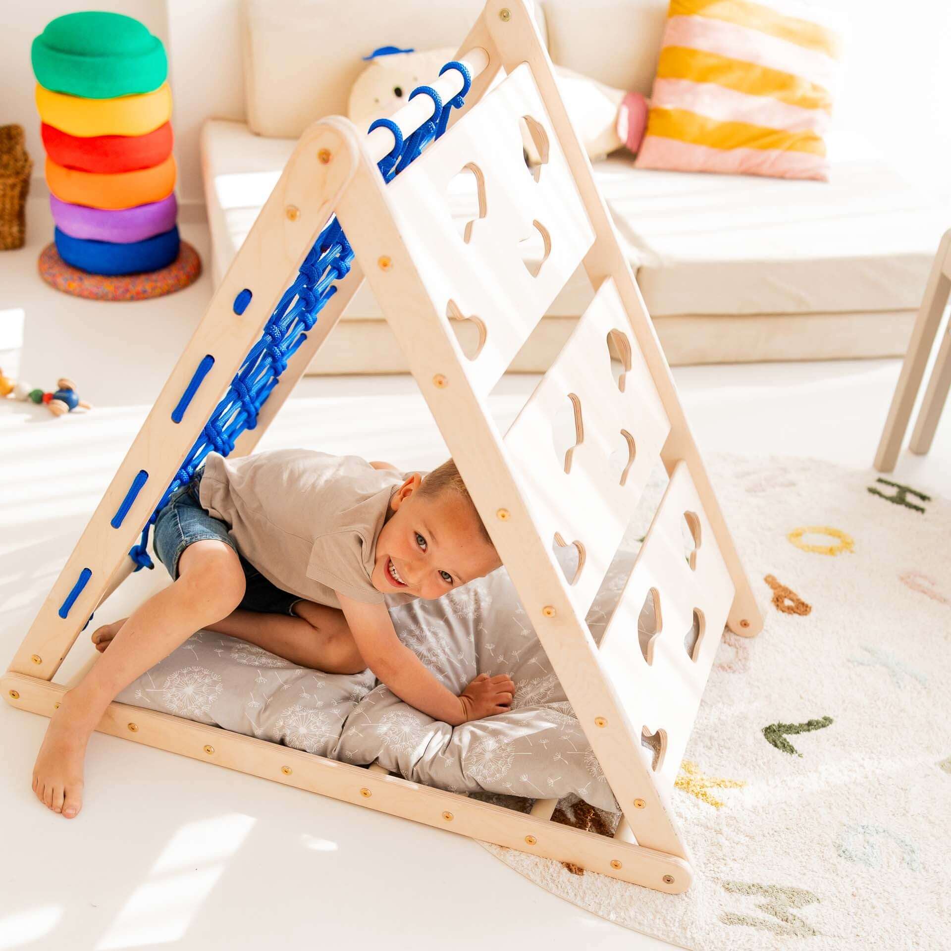 Ein lächelndes Kind spielt im Kletterdreieck Äffchen mit Sprossen und Netz in einem hellen Kinderzimmer.