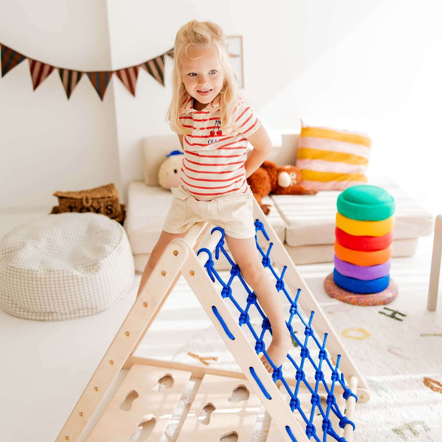 Ein Kind klettert fröhlich auf einem Kletterdreieck Äffchen mit Sprossen und Netz im Spielzimmer.