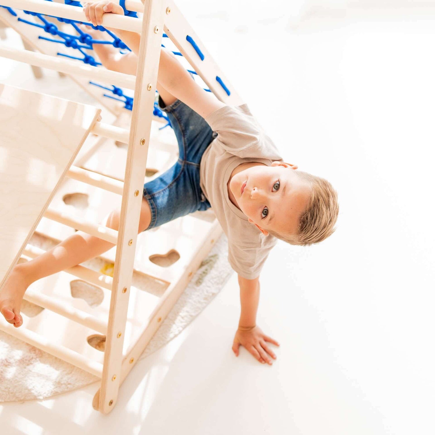 Junge spielt an einem Kletterdreieck aus Holz, Teil des Klettersets Äffchen, entwickelt Bewegungsfähigkeiten.